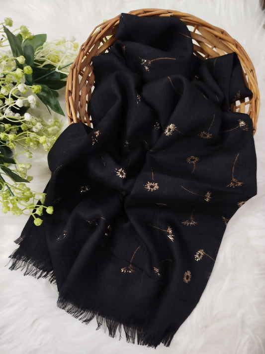 Black scarf with floral patterns draped over a woven basket on a white surface with greenery.