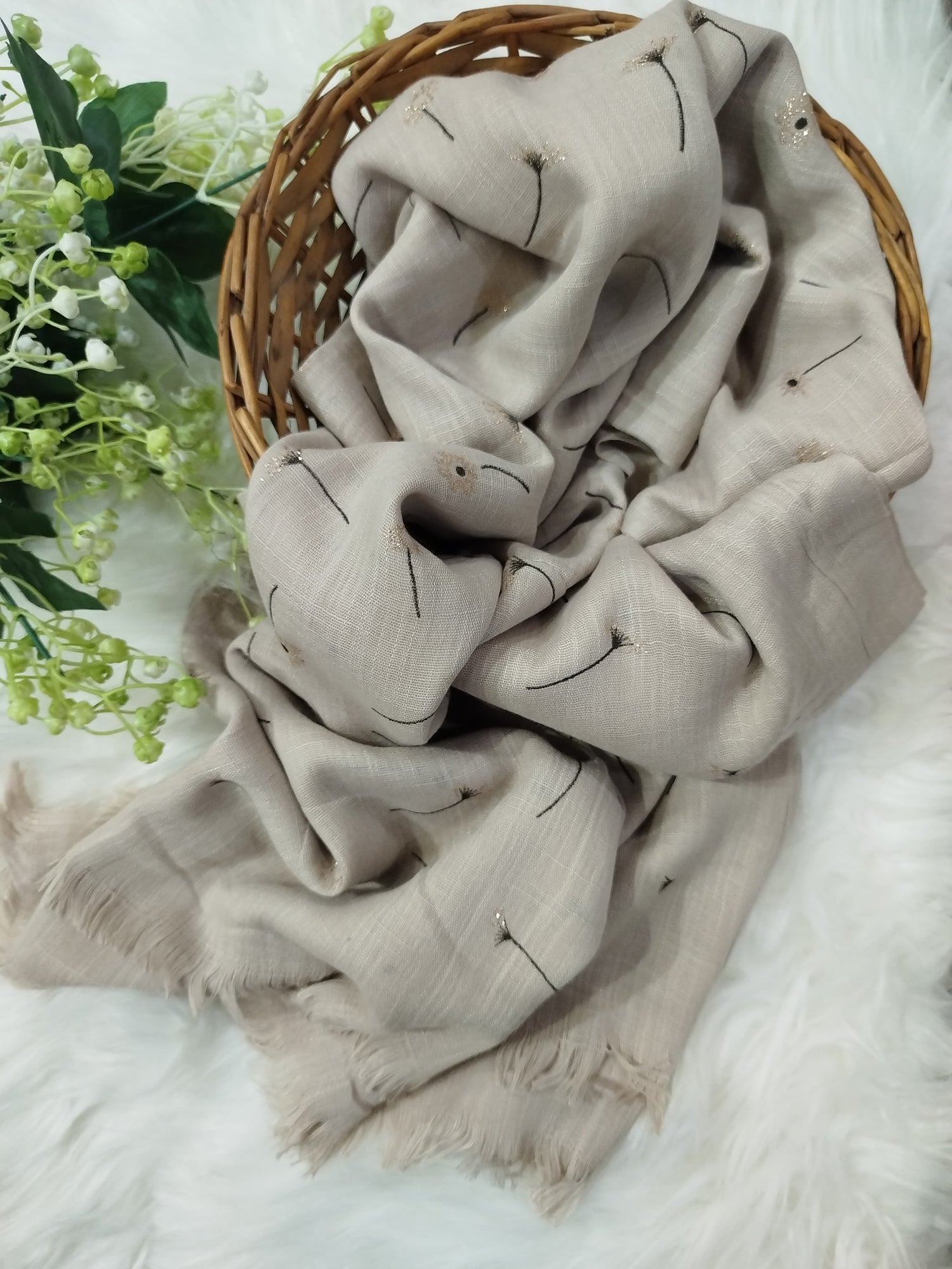 Beige blanket with smiley face patterns draped over a wicker basket on a white surface with greenery.