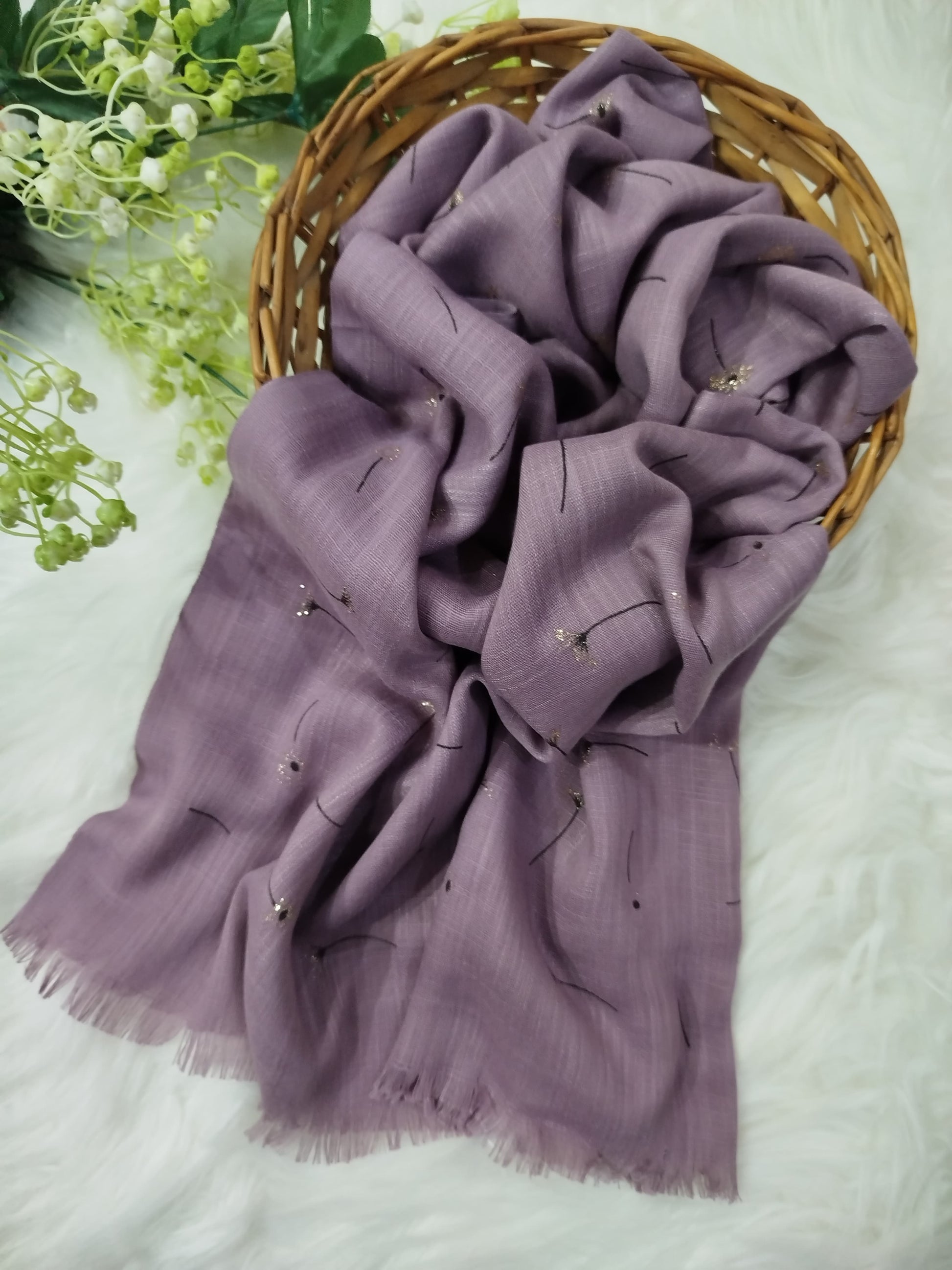 Purple scarf with floral embroidery on a white surface with greenery