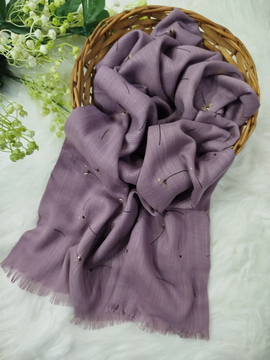 Purple scarf with floral embroidery on a white surface with greenery