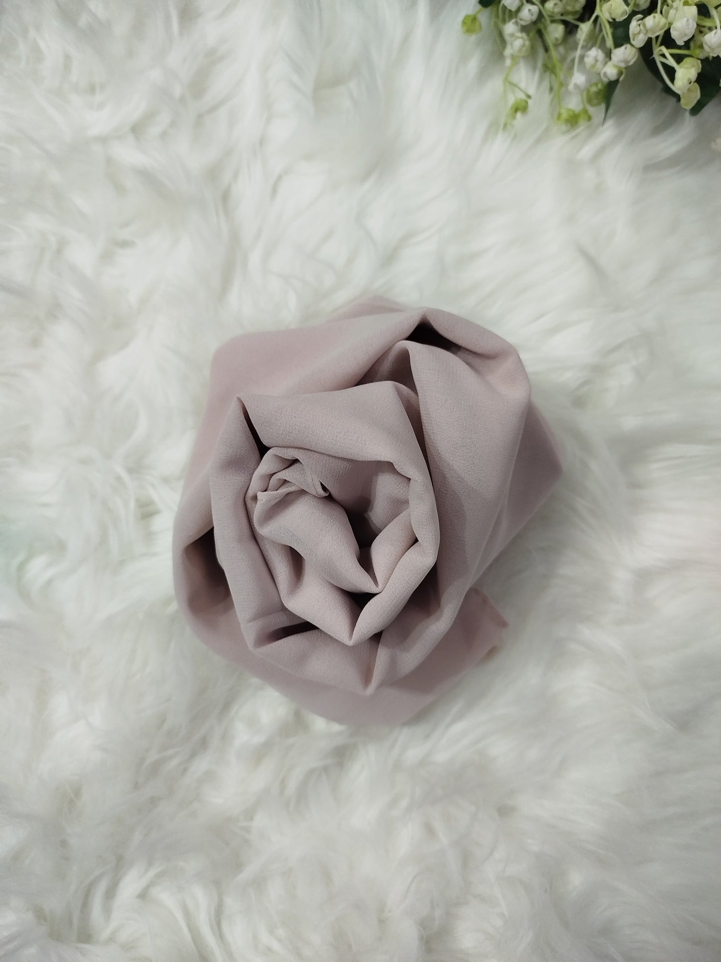 Folded light purple fabric on a white textured surface with greenery at the top corner.