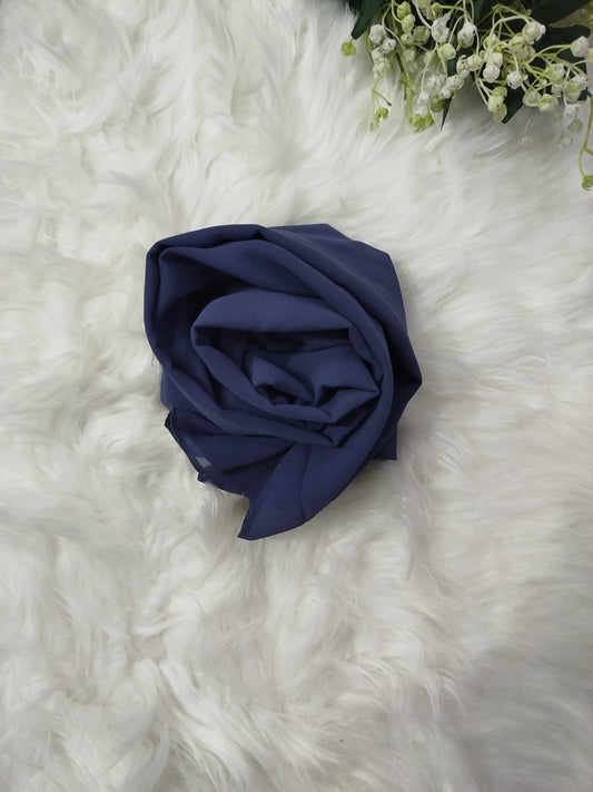 Navy blue fabric flower on a white fluffy surface with greenery.
