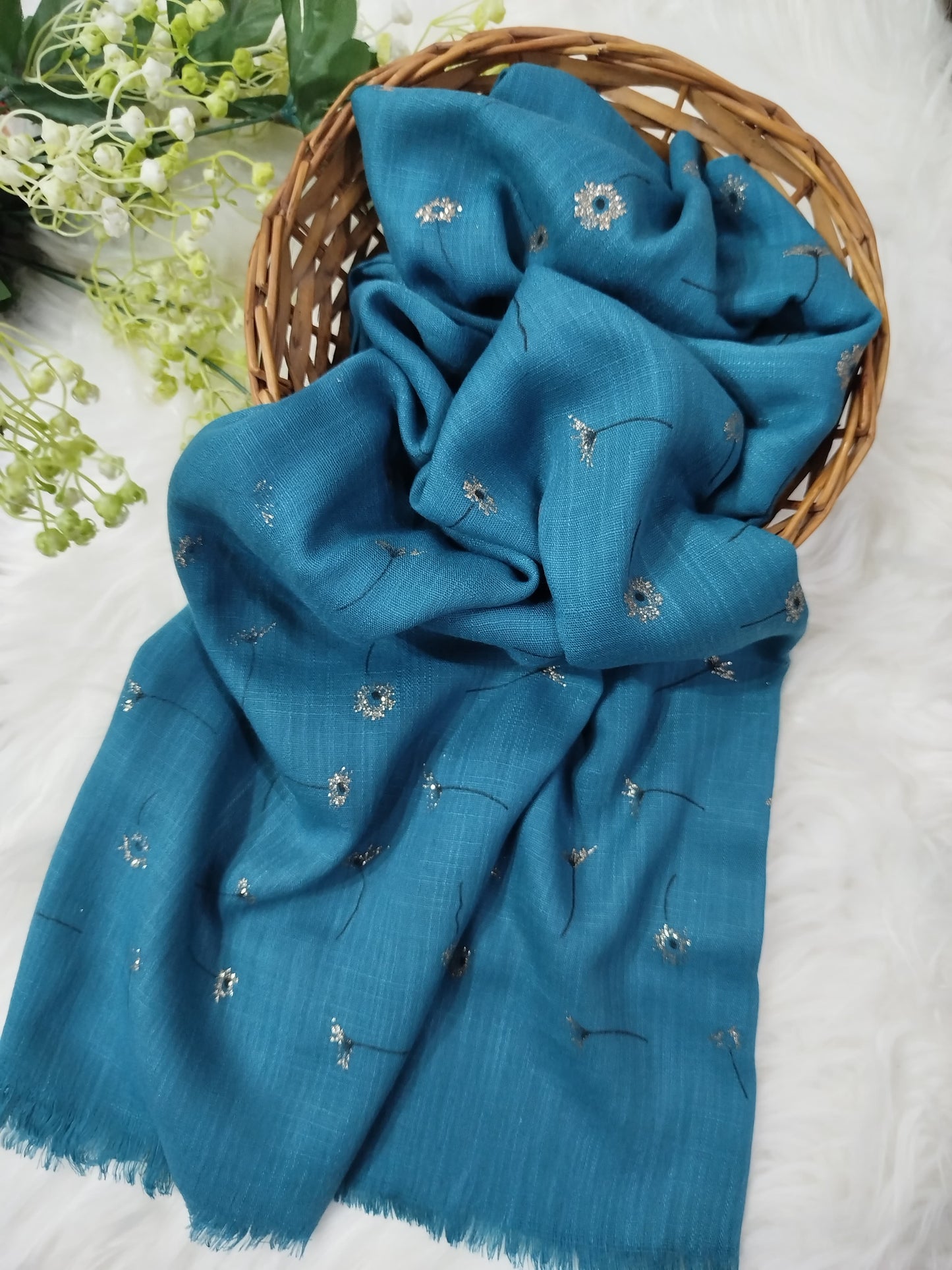 Blue scarf with floral embroidery on a white surface with greenery