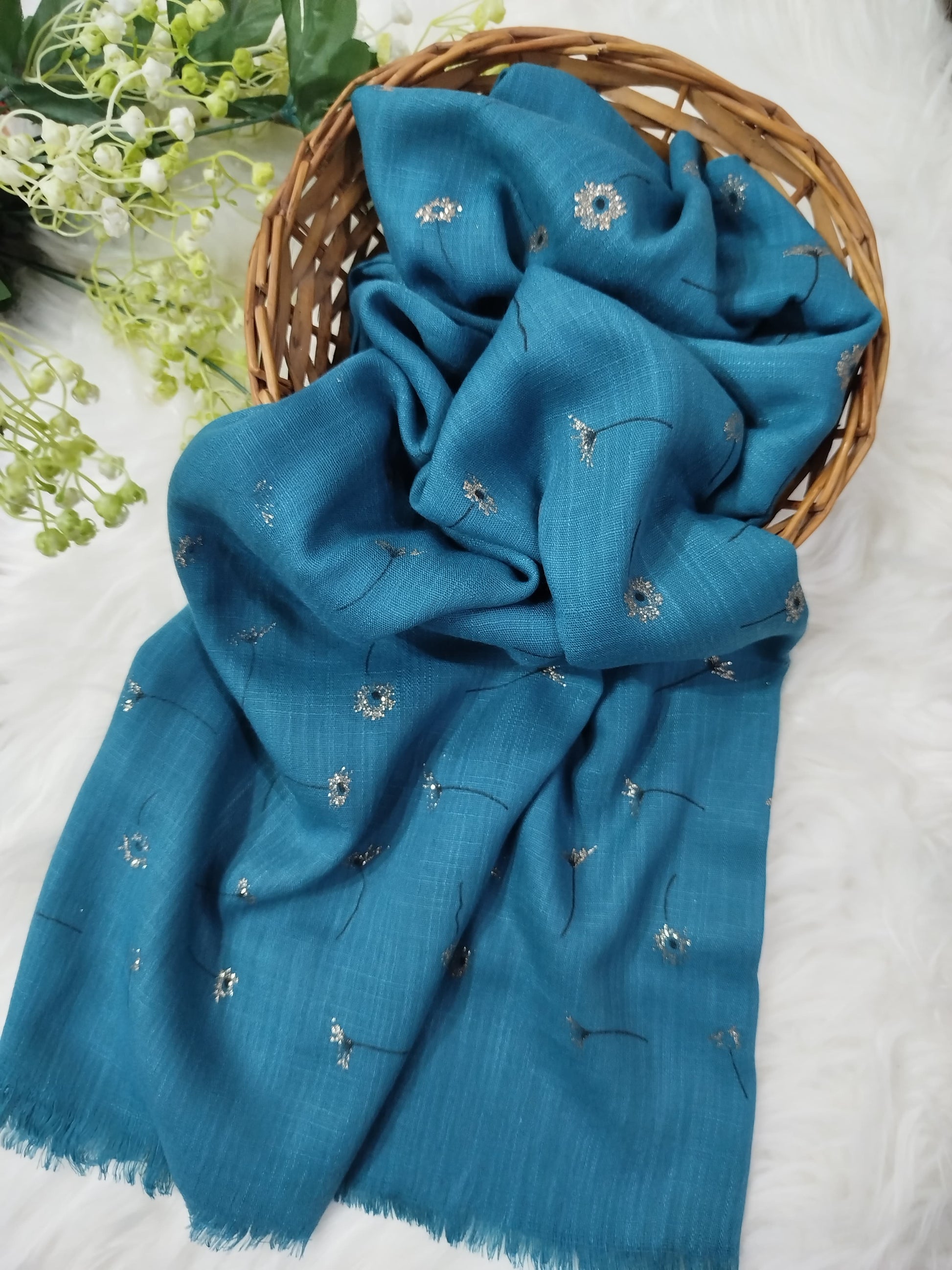 Blue scarf with floral embroidery on a white surface with greenery